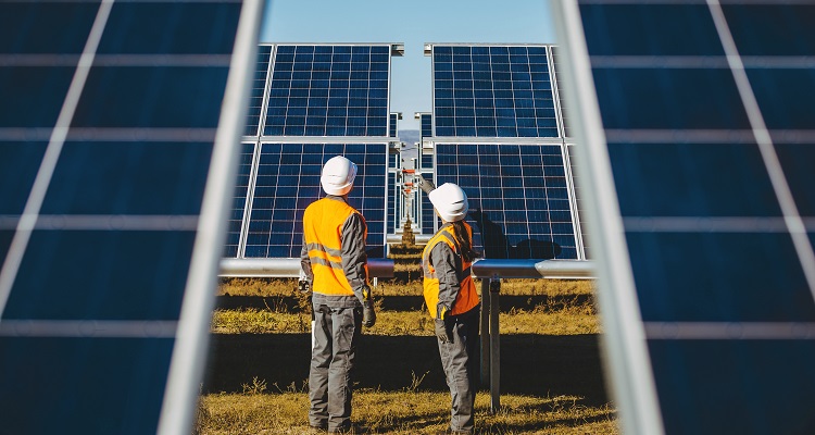 Two workers inspecting large solar panels. 