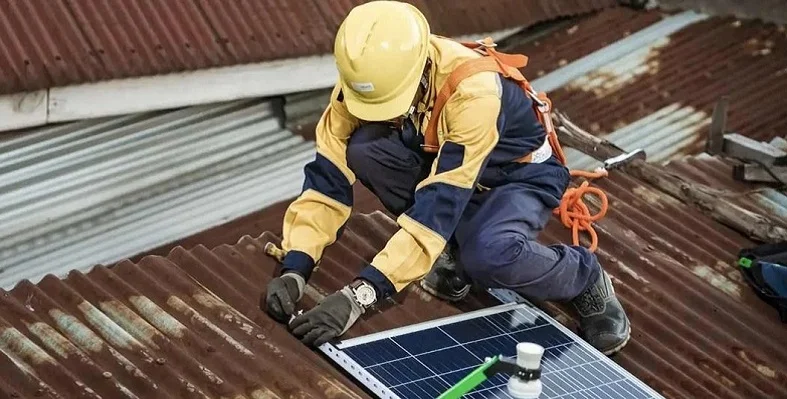 An engineer fixing a solar panel to a rust-covered roof. 