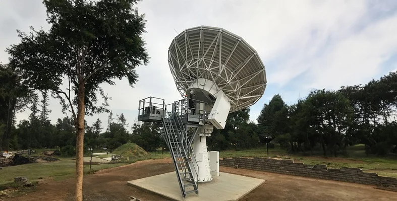 A large satellite set up pointing at the sky in a wooded area.