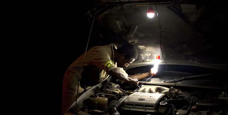 An African engineer working on a vehicle engine by light at night.