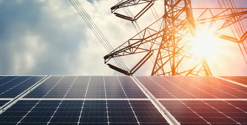 Solar panels in the foreground with energy transmission lines in the background.