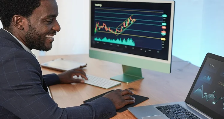 A business man sitting at a desk with financial data on his screen.