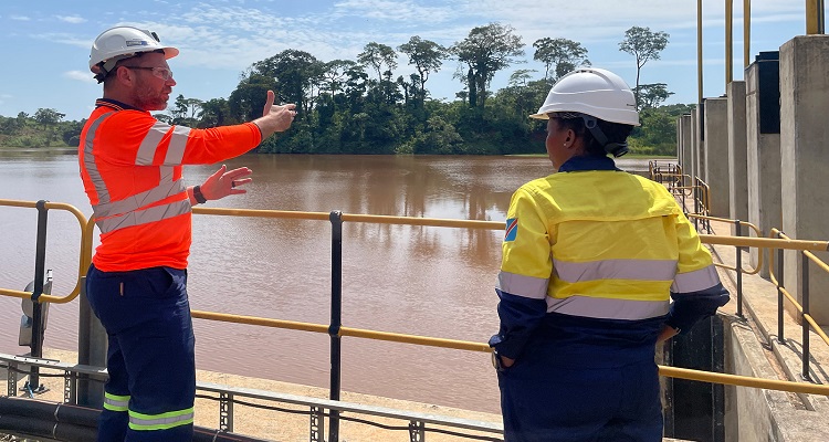 Two personnel in hard hats surveying a dam. 
