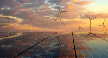 An image depicting solar panels in the foreground with wind turbines behind. 