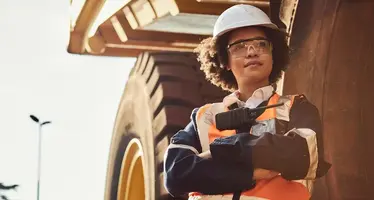 A female miner standing in front of a dump truck. 
