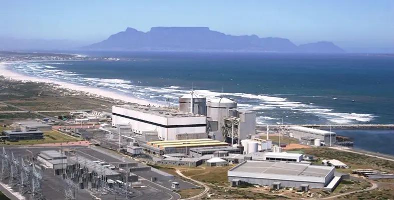 A wide shot of the Koeberg facility on the coast in Cape Town with Table Mountain in the background.