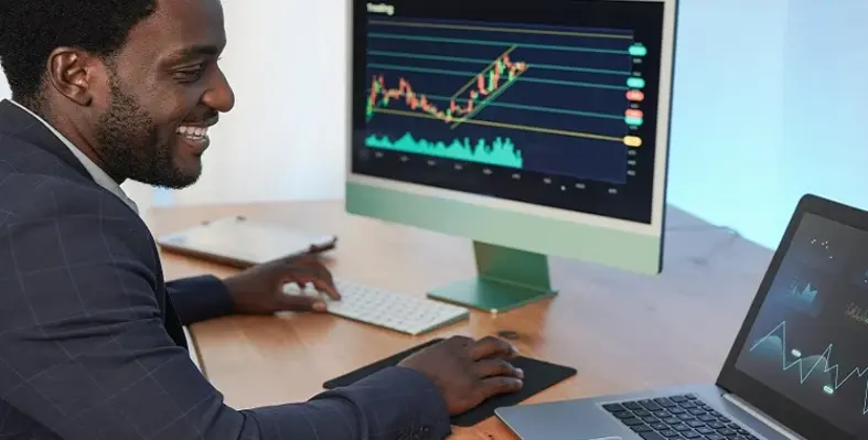 A business man sitting at a desk with financial data on his screen.