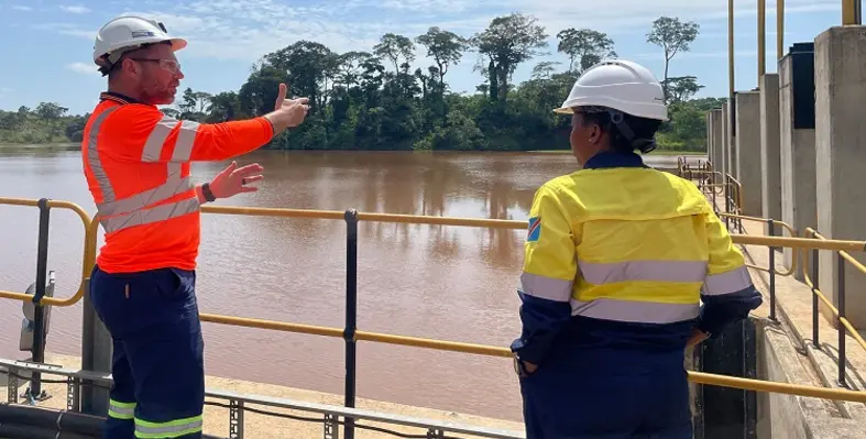 Two personnel in hard hats surveying a dam. 