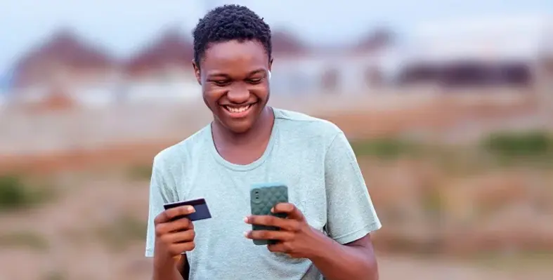 An African man looking at his phone and credit card.