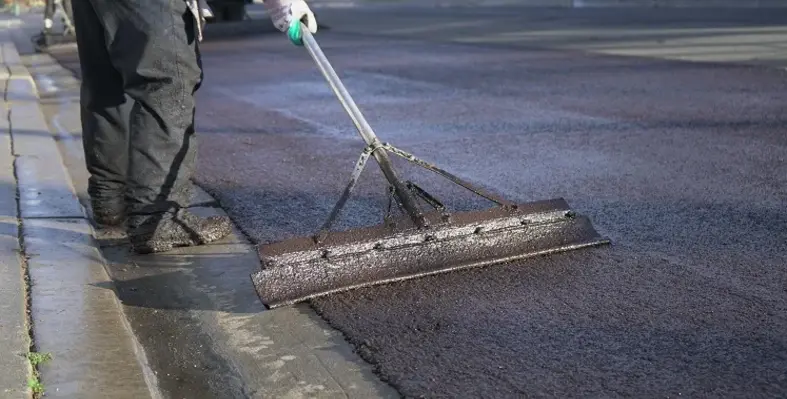 A worker laying fresh slurry seal on a road. 
