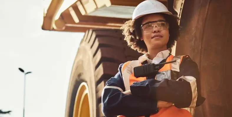 A women miner standing in front of a large piece of machinery. 
